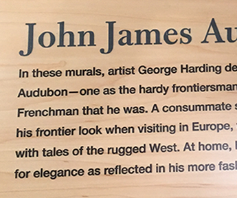 A closeup of a reader rail at the Audubon House showing text printed on wood with low light glare.